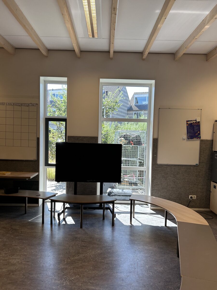 Ruimte in een schoolgebouw met tafels en een scherm